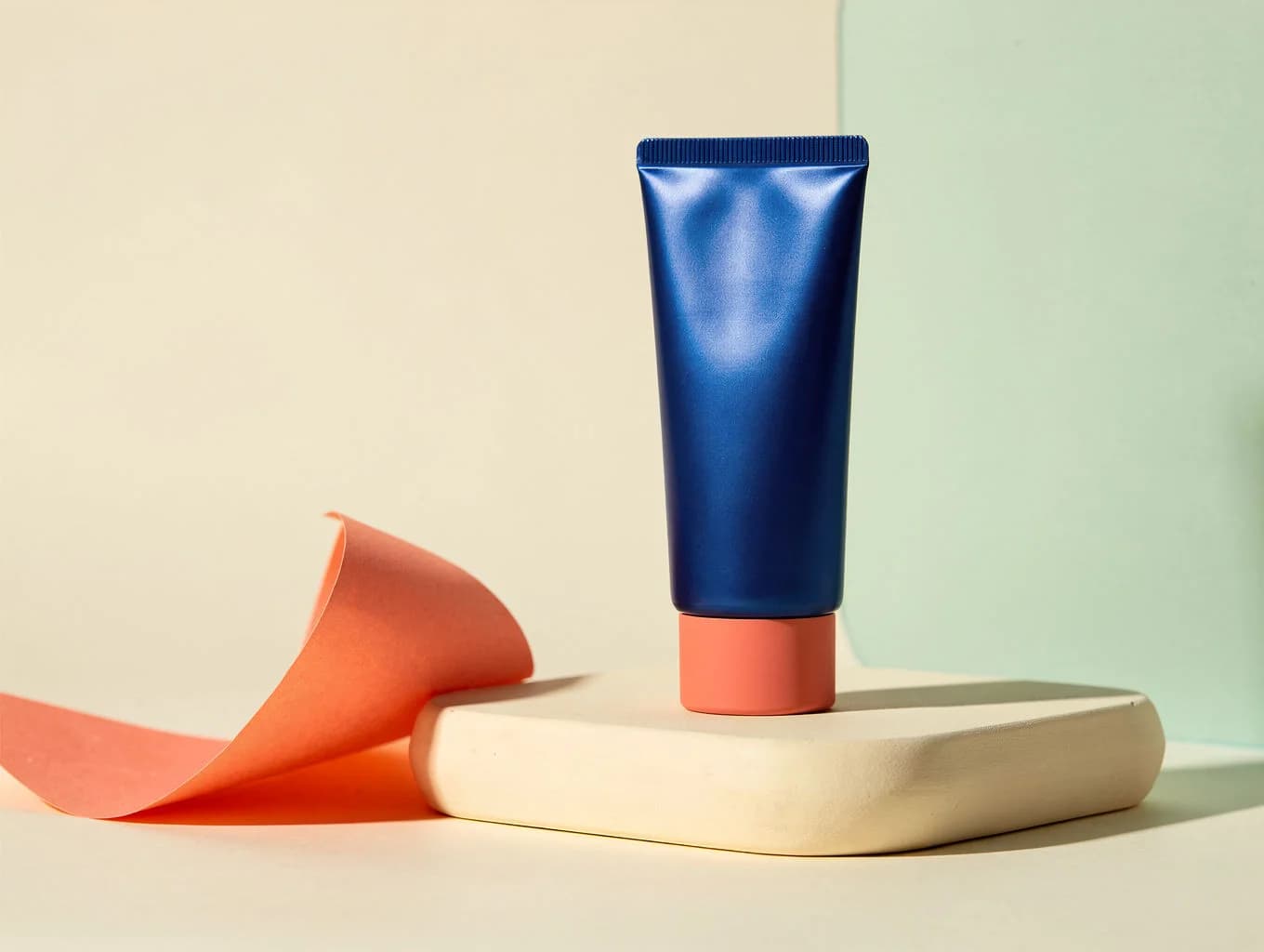 Studio product photograph of an unbranded blue cosmetic tube with coral and mint accents